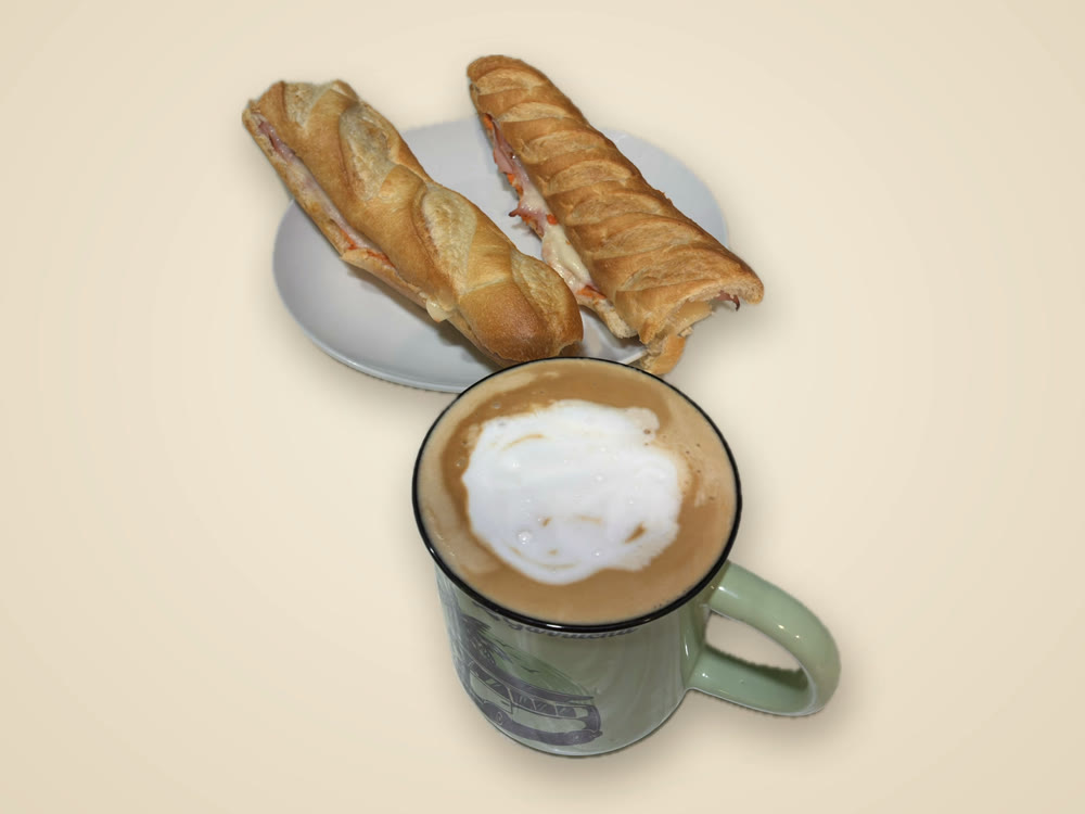 Dos bocadillos de jamón y queso en plato, con una taza de café con leche