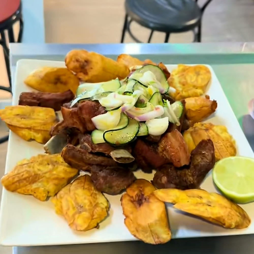 Plato de carne frita con patacones, curtido de pepino y cebolla, y limón